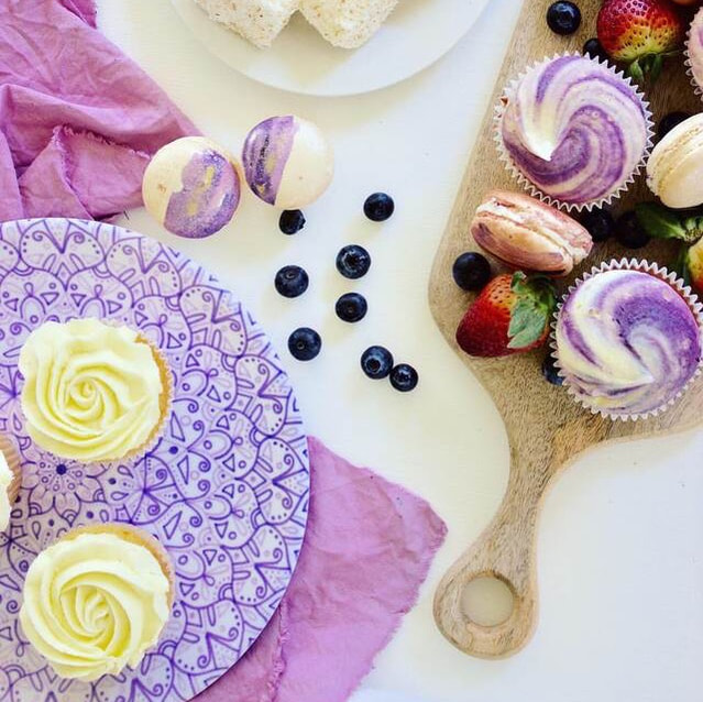 Decorative textiles styled with purple cupcakes, fresh strawberries and homemade macarons