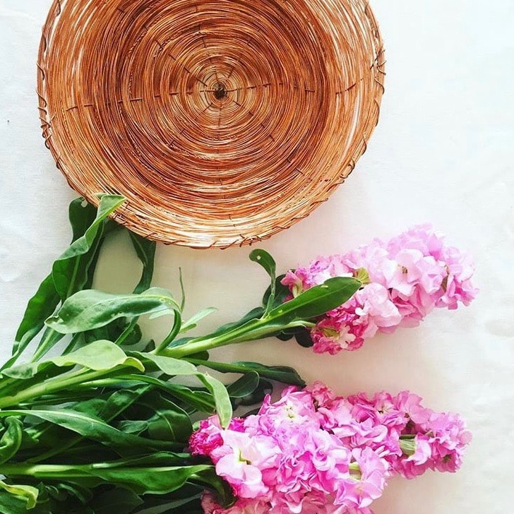 Woven copper plate paired with bright pink flowers and greenery